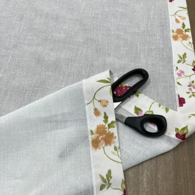 Primo piano bordura floreale multicolore su tendina bianca con forbici