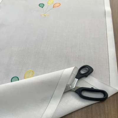 Taglio sartoriale della tendina a vetro per cameretta con ricamo palloncini e rifinitura laterale.