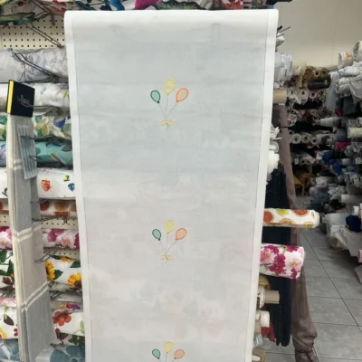 Tendina a vetro bianca con motivo a palloncini esposta verticalmente in un negozio di tessuti.