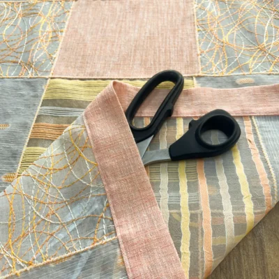 Dettaglio della cucitura laterale e del bordo di una tendina a vetro rosa pesca con forbici da sarto