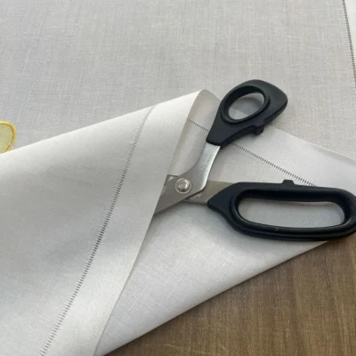 Dettaglio del tessuto bianco effetto lino della tendina a vetro con bordo a punto a giorno rifinito.